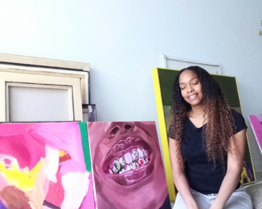 Jomad, a female artist, kneeling in front of artworks in her gallery