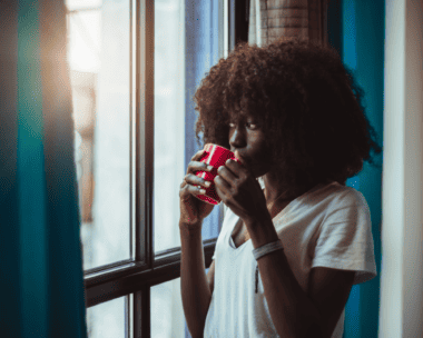 A dark skin lady behind a window with a cup of Ghanaian beverage