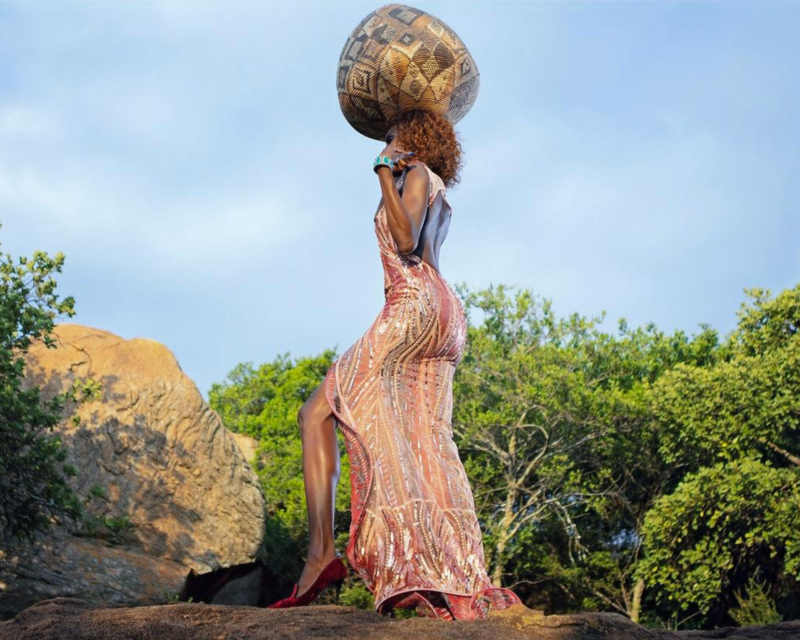 Fashion designer Liz Ogumbo posing with a unique Ilala Basket, showcasing her collection, in a creative photo by @Photoworxrsa emphasizing It's Not A Pot, It's A Basket!
