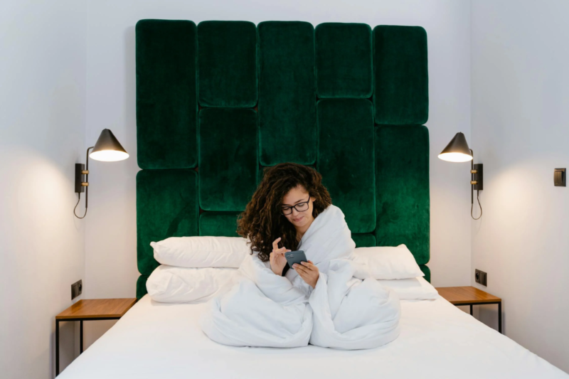A lady on a velvet bed pressing her smartphone