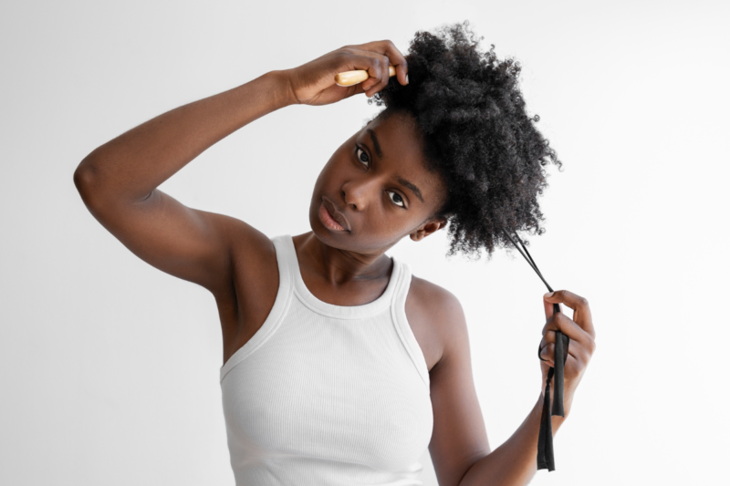 A close up of a dark skinned lady experiencing hair breakage styling her hair.