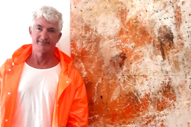 Portrait of Ulrich Gottlieb, a renowned physical theatre artist, smiling warmly with a painting behind him
