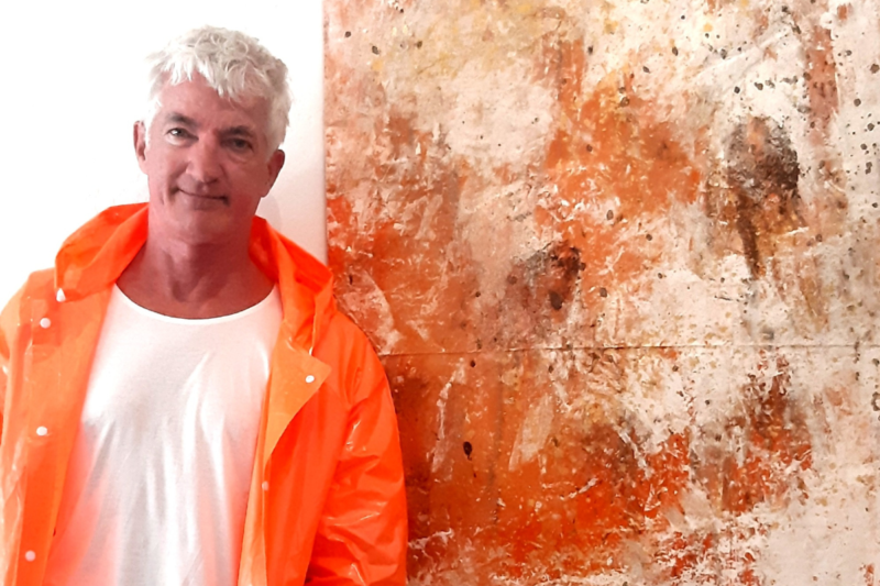 Portrait of Ulrich Gottlieb, a renowned physical theatre artist, smiling warmly with a painting behind him