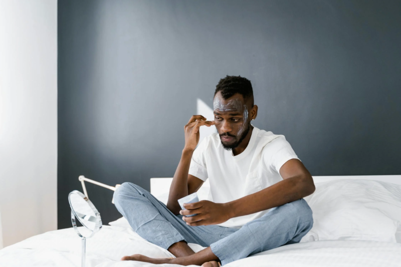 A Man Looking at the Mirror while Applying Face Cream. Covering an article on What men should look for in skincare ingredients