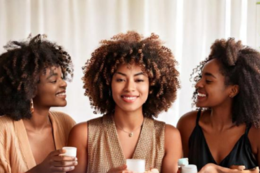 A diverse group of women with natural hair (curls, coils, afros) using affordable hair care products in a bright, relaxing environment.