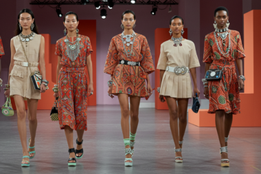 A vibrant and futuristic fashion scene showcasing a dynamic runway filled with bold accessories from 2025 trends. Include models adorned with statement pieces like oversized necklaces, chandelier earrings, and cultural jewelry, alongside cutting-edge smart accessories such as solar-powered clutches and LED-embedded footwear.
